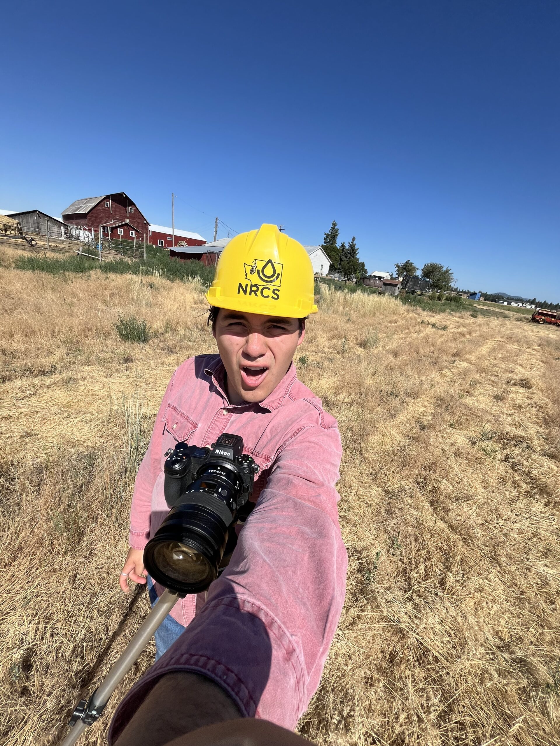 Kyle smiling while taking photos in the field. Another aspect of public affairs is creating media for projects, this one was documenting NRCS-WA’s soil sample drilling rig, and the people who were working on it.